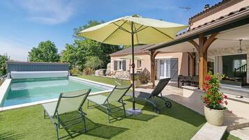 Une piscine avec des chaises longues, un patio couvert et une maison avec un toit en tuiles.