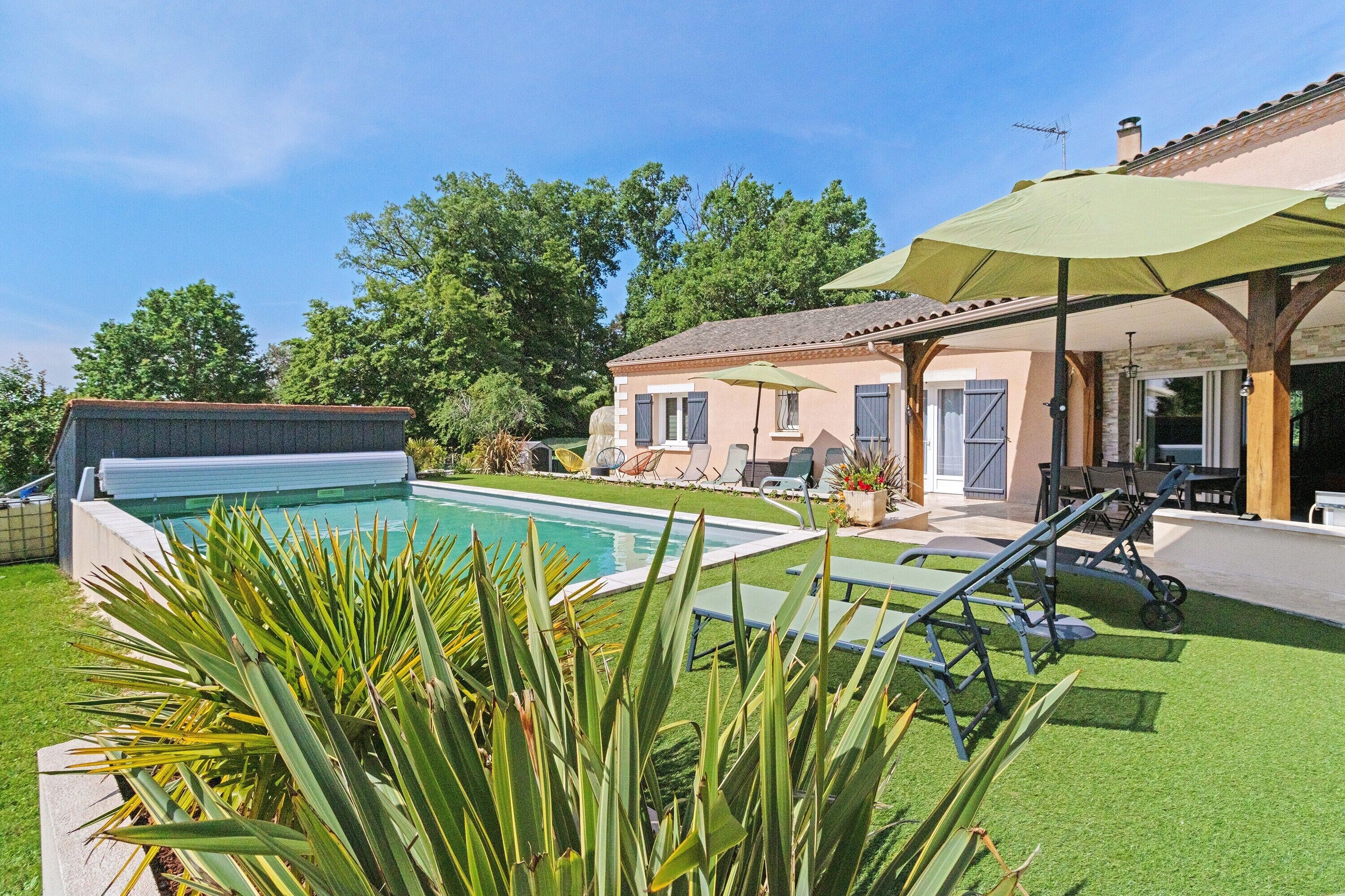 A poolside area with a covered seating area, a pool, and a house in the background.