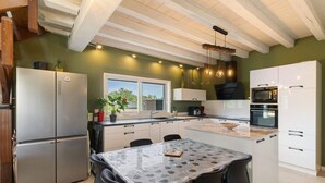 A modern kitchen with a central island, stainless steel appliances, and a view to the outside.