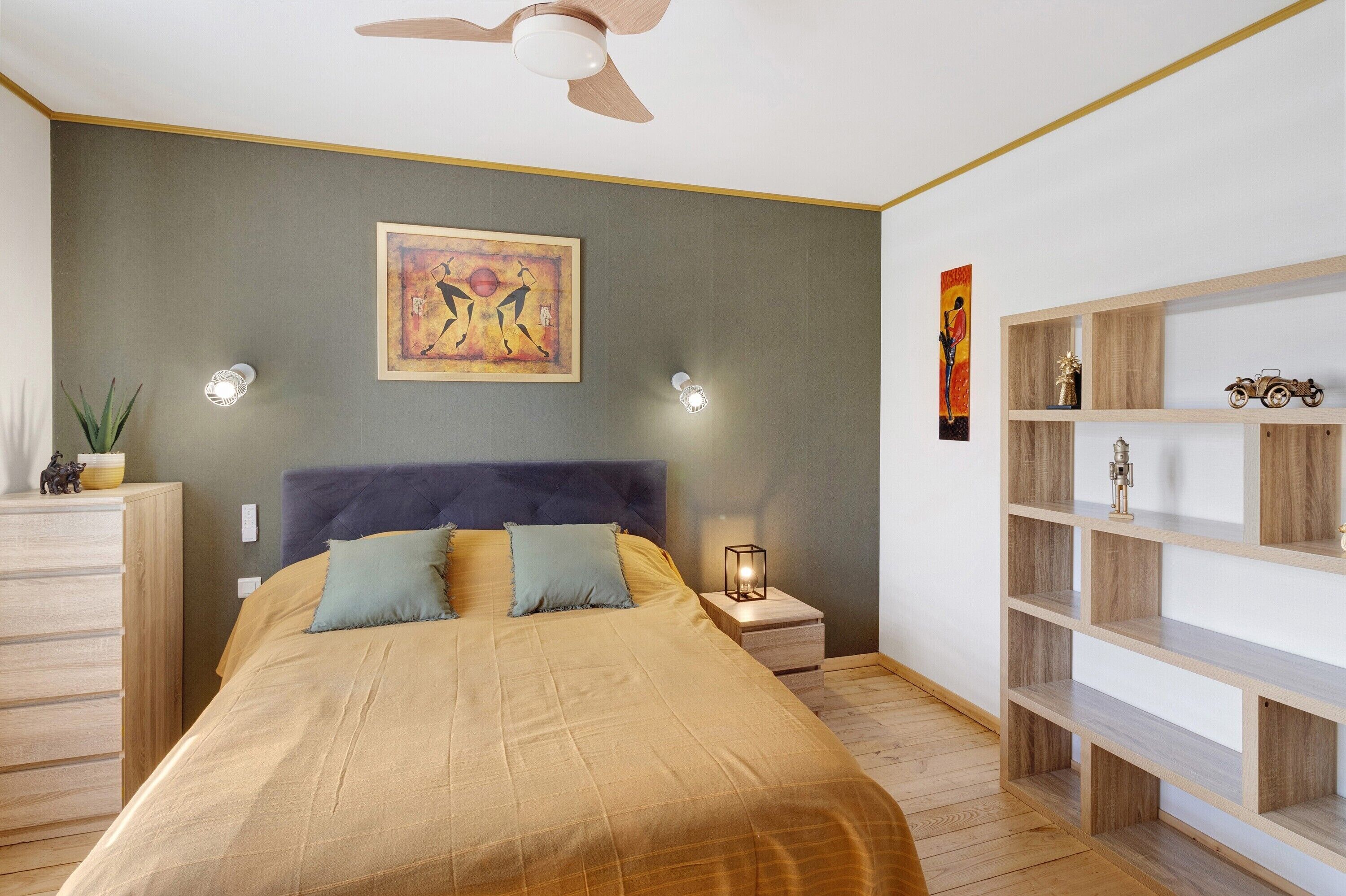 Ein Schlafzimmer mit einem Bett, einem Nachttisch, einem Wandregal und einem Deckenventilator.