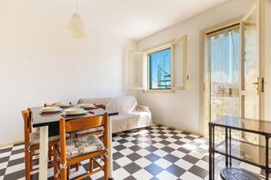 Ein Essbereich mit einem Tisch für vier Personen, einer Couch, einem Schachbrettmuster-Boden und einem Balkon mit Aussicht.