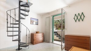 A room with a spiral staircase, a wooden dresser, a wicker chair, and a sliding glass door leading to an outdoor area. - Villetta Sole e Sale - Trilo by BarbarHouse (Campomarino)
