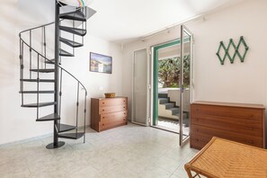 A room with a spiral staircase, a wooden dresser, a wicker chair, and a sliding glass door leading to an outdoor area. - Villetta Sole e Sale - Trilo by BarbarHouse (Campomarino)