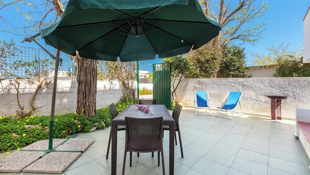 An outdoor patio with a table and chairs, a green umbrella, and a blue lounge chair. - Villetta Sole e Sale - Trilo by BarbarHouse (Campomarino)