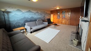 Ett mysigt vardagsrum med en grå soffa, en svart fåtölj, en vit matta och en väggpanel av trä med inramade bilder.