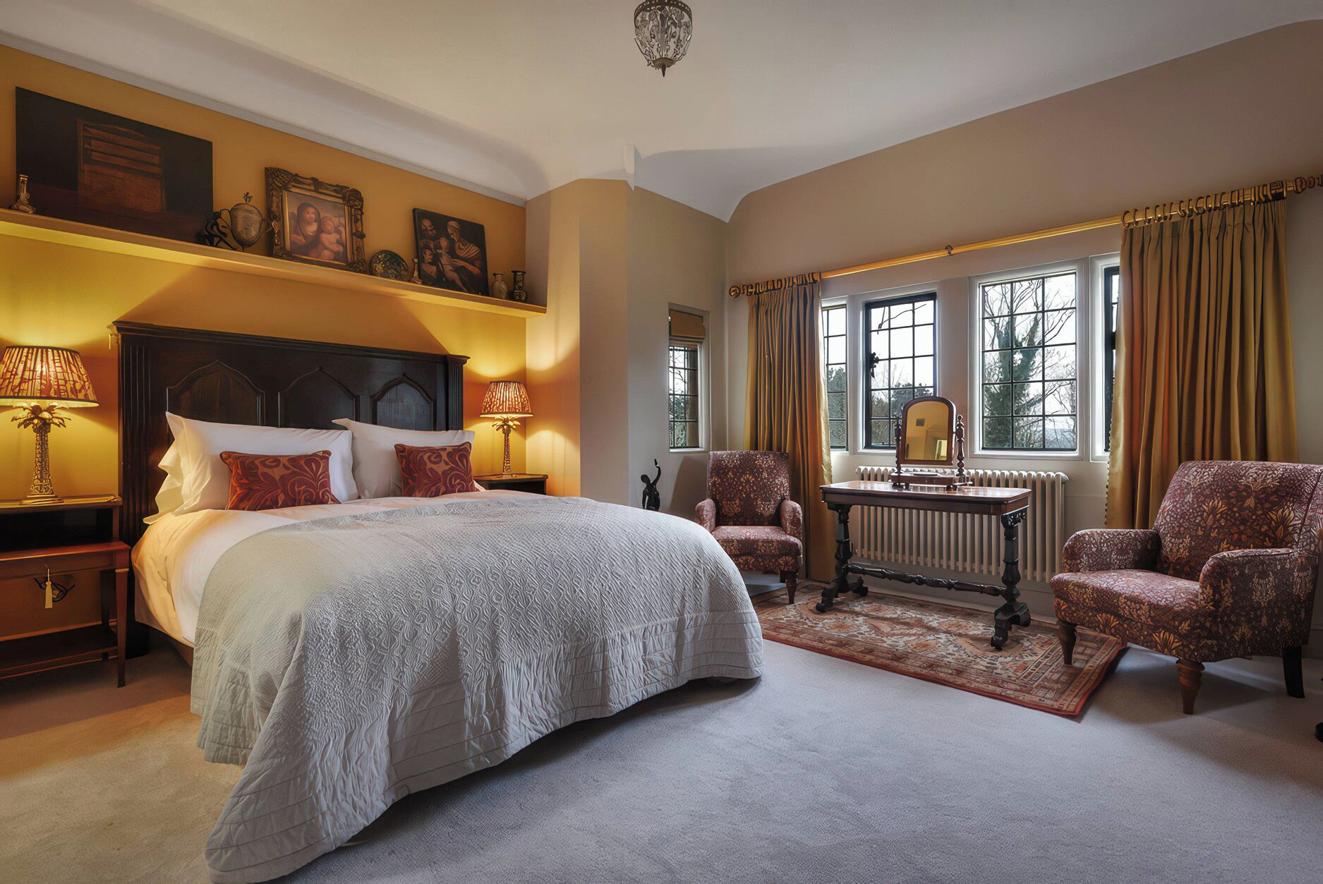 A spacious bedroom with a large bed, two armchairs, a table with a mirror, and a radiator.