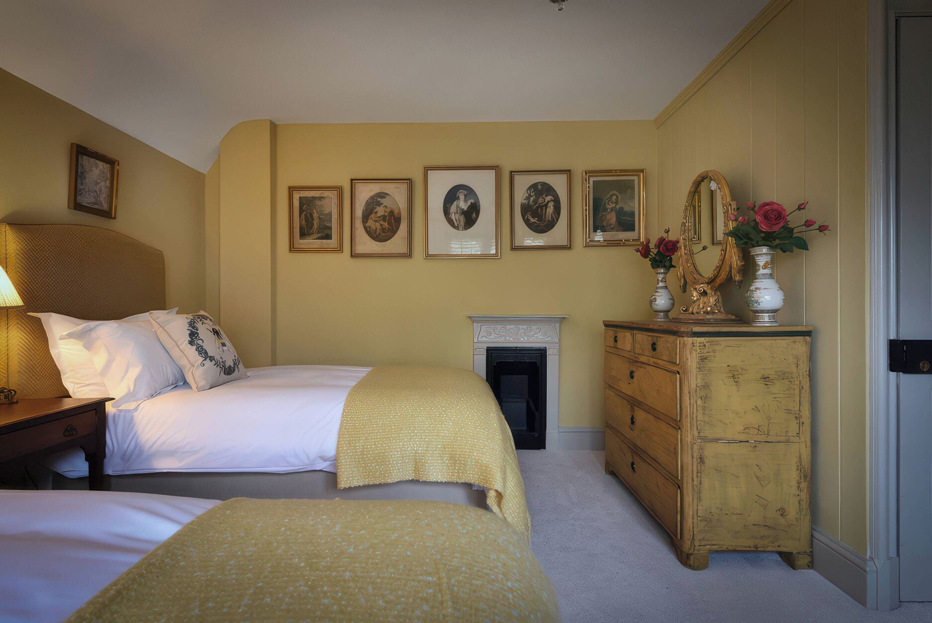 A bedroom with two beds, a dresser, a mirror, and a fireplace.
