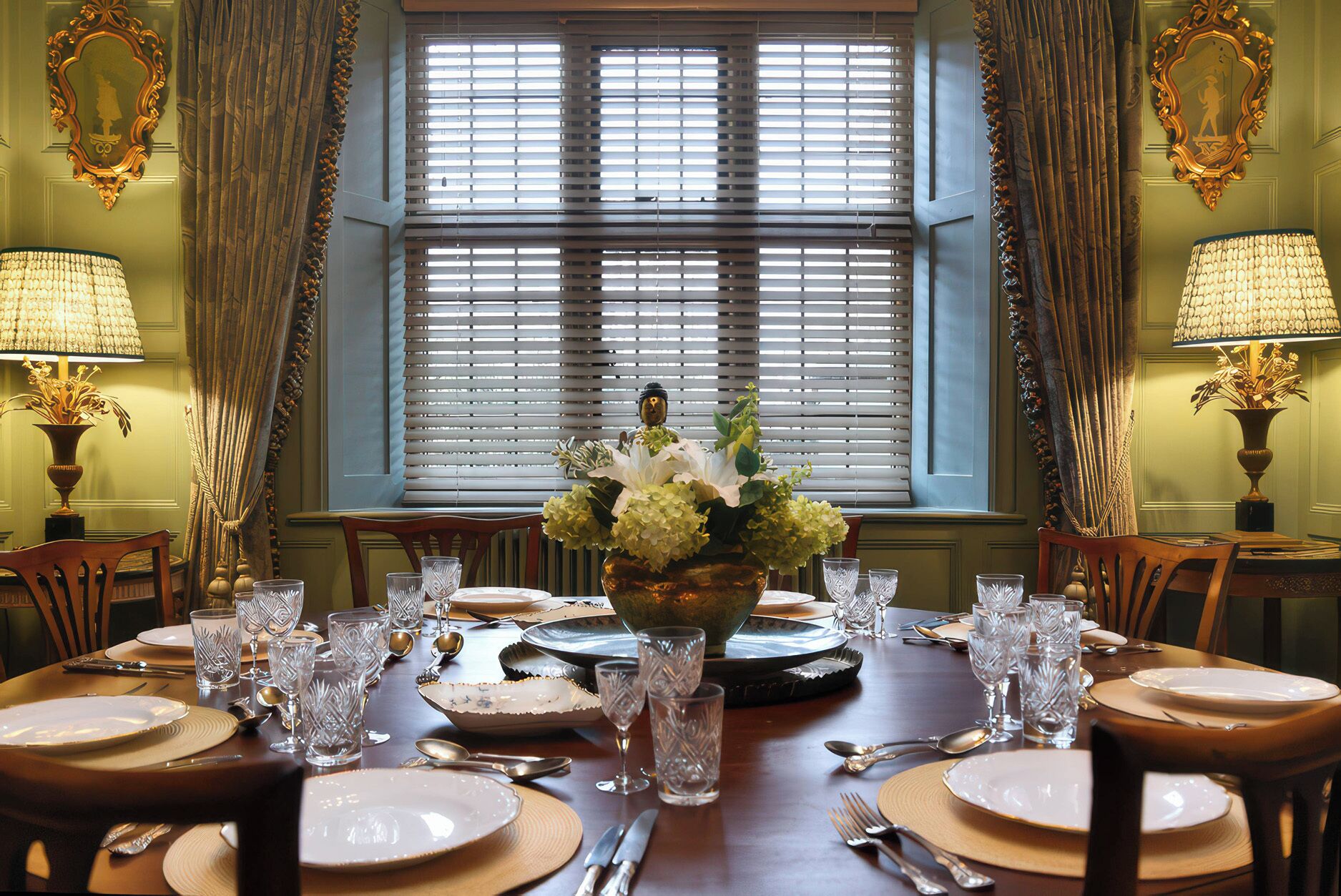 A dining table set for a meal with a vase of flowers, surrounded by chairs and lamps.