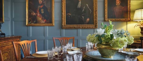 A dining room with a table set for four, three framed portraits on the wall, and a vase of flowers on the table.