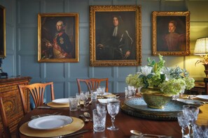 A dining room with a table set for four, three framed portraits on the wall, and a vase of flowers on the table. - Morland Manor (Peterborough)