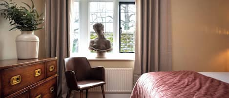 A bedroom with a bed, a chair, a dresser, a window with curtains, and a statue.
