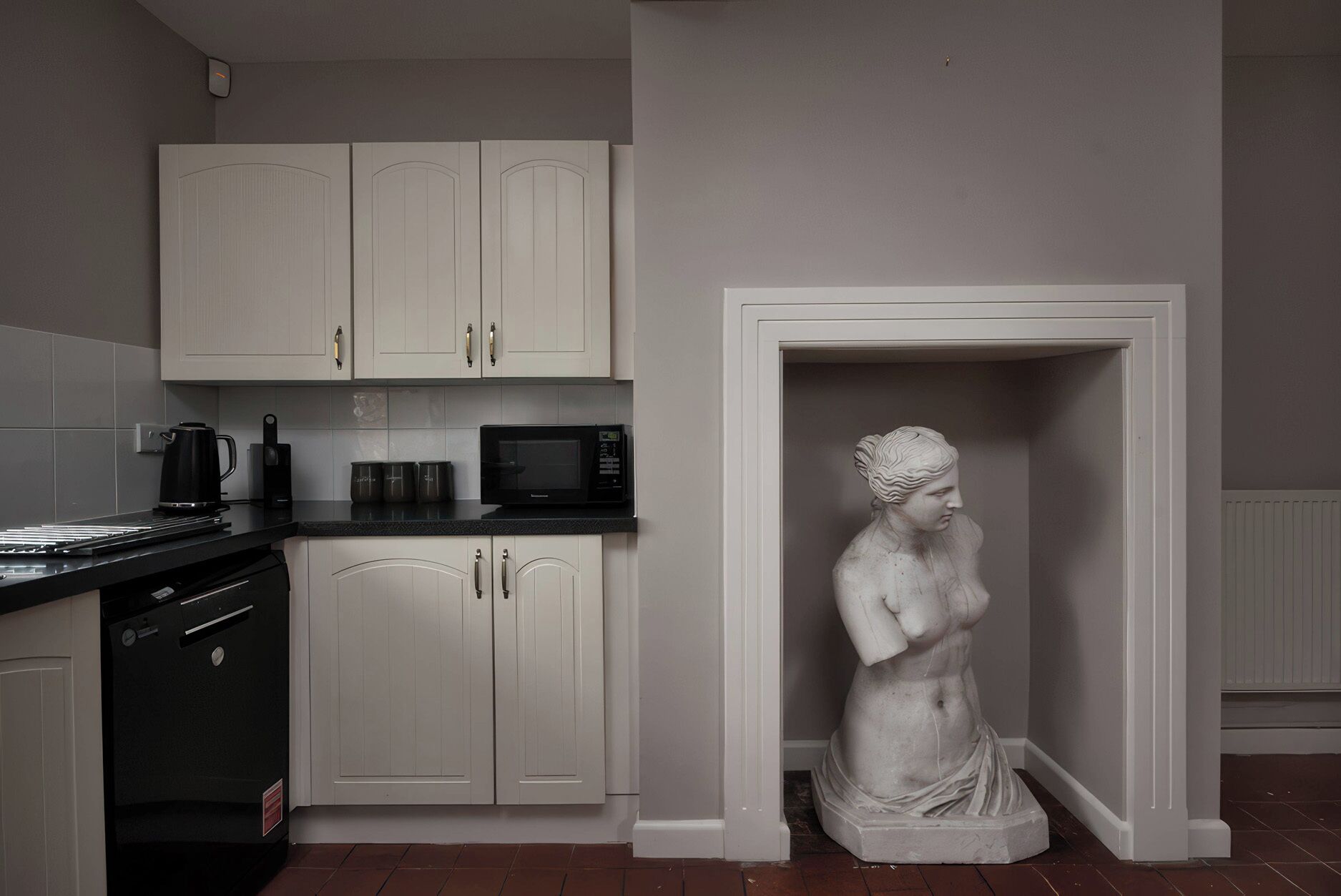 Une cuisine moderne avec des meubles blancs, un four à micro-ondes et une statue de femme.