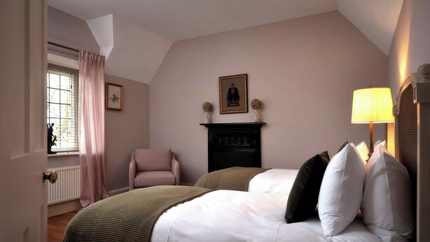 Una camera da letto con un letto, una sedia, un camino e una finestra con tende.