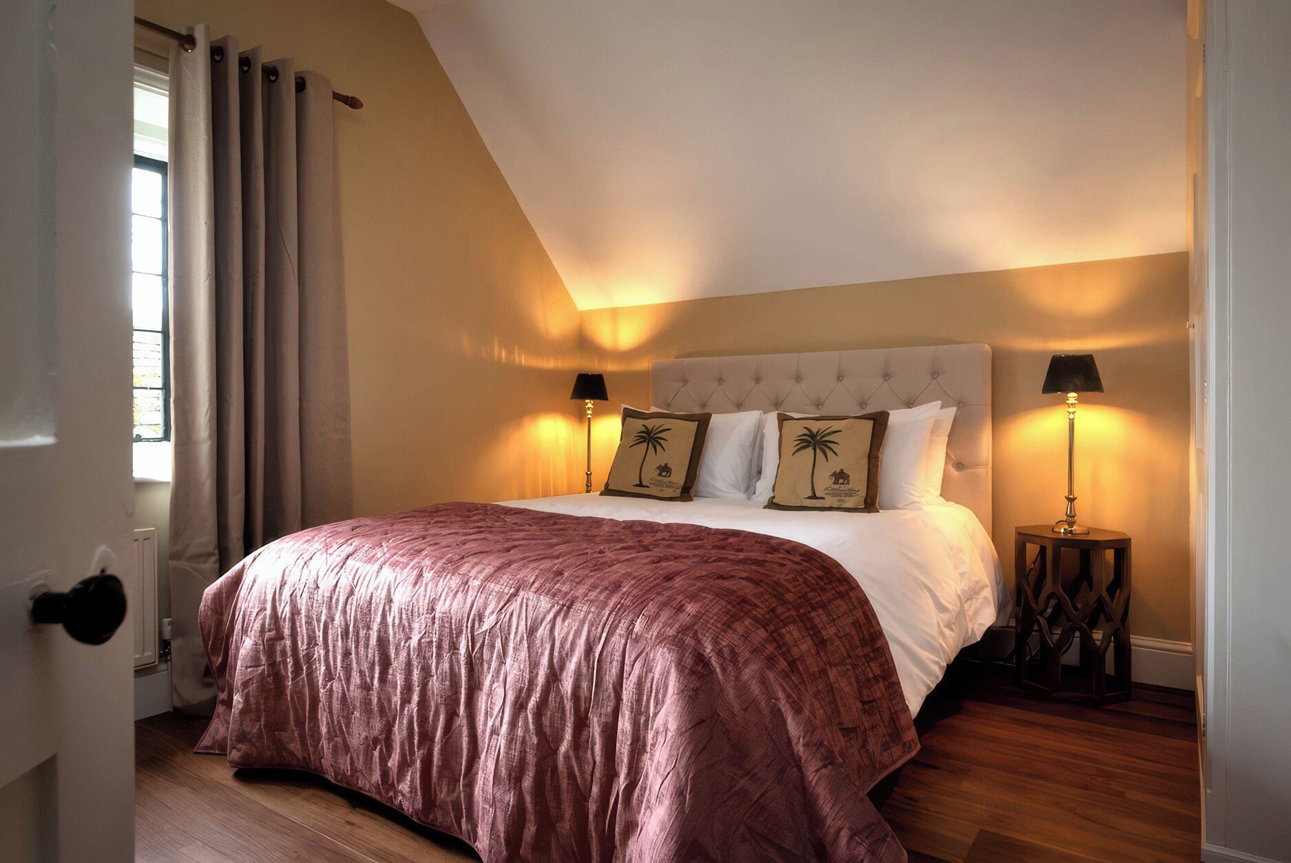 Een slaapkamer met een groot bed, twee bedlampen en een raam met gordijnen.