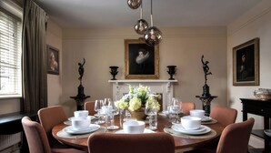 Una sala da pranzo formale con un tavolo rotondo apparecchiato per sei persone, affiancato da due statue nere, un camino e ritratti appesi alle pareti.