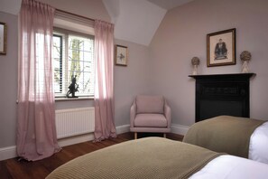 A bedroom with a window, a chair, a fireplace, and two beds. - The Gatehouse (Peterborough)