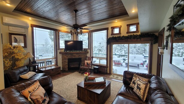 A cozy living room with leather sofas, a fireplace, a television, and large windows with a snowy view. - Hot tub, mtn views, massage chair, & steam shower! (Divide)