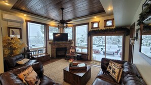 A cozy living room with leather sofas, a fireplace, a television, and large windows with a snowy view. - Hot tub, mtn views, massage chair, & steam shower! (Divide)