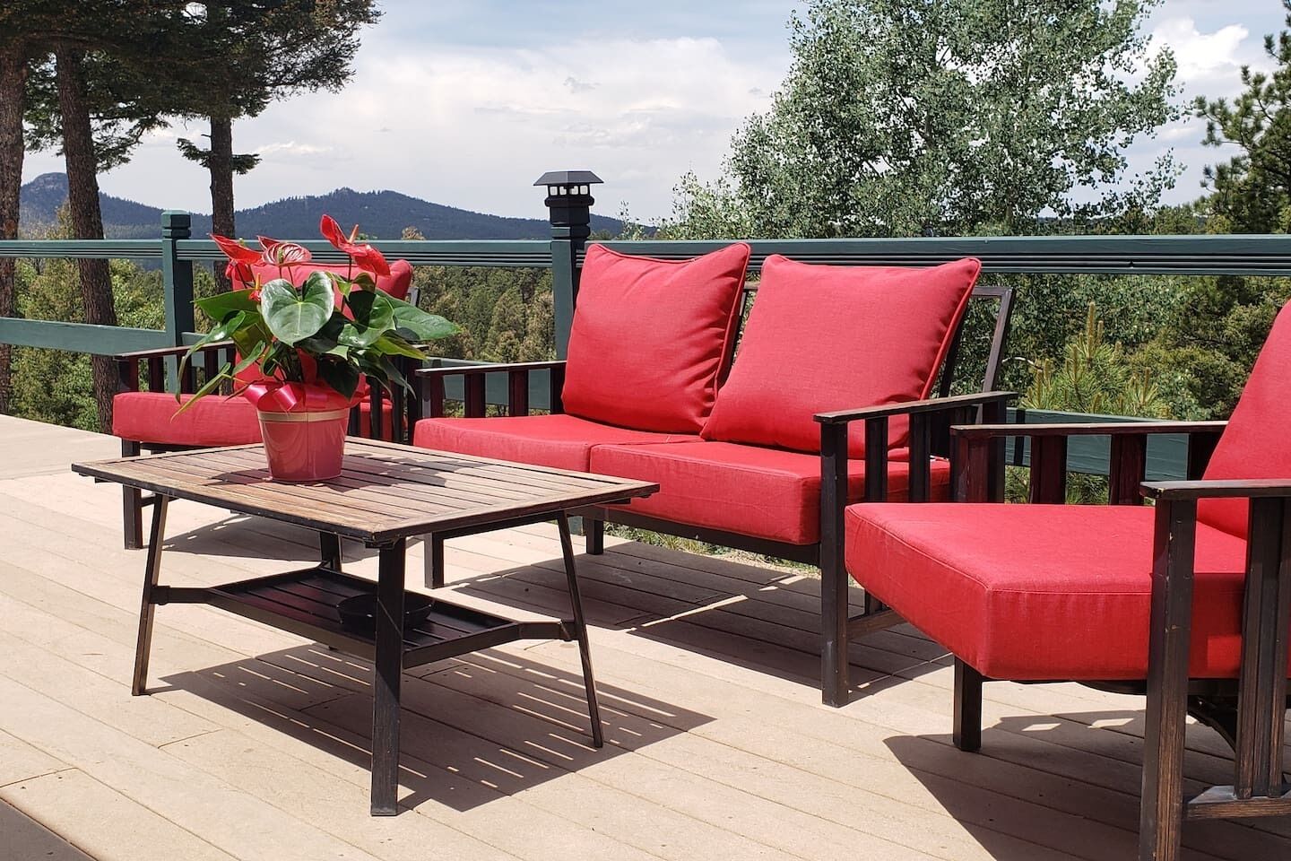 A deck with a wooden table, red cushioned seating, and a potted plant.
