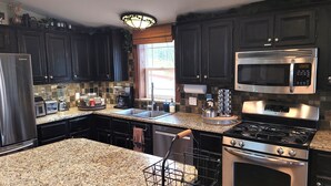 A kitchen with dark cabinets, granite countertops, a stainless steel refrigerator, a microwave, a stove, and a coffee maker. - Hot tub, mtn views, massage chair, & steam shower! (Divide)