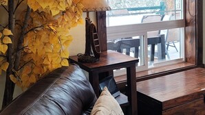 A cozy room with a leather couch, a table with a lamp, and a window overlooking a snowy landscape. - Hot tub, mtn views, massage chair, & steam shower! (Divide)