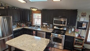 A modern kitchen with dark cabinets, stainless steel appliances, granite countertops, and a skylight. - Hot tub, mtn views, massage chair, & steam shower! (Divide)