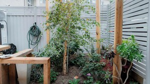 A garden with a wooden trellis supporting a climbing plant, surrounded by various potted plants and a wooden table. - Peace and Love 2 BDR Townhouse West Melbourne (West Melbourne)