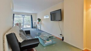 A modern living room with a glass coffee table, a black sofa, and a flat-screen TV mounted on the wall. - Peace and Love 2 BDR Townhouse West Melbourne (West Melbourne)