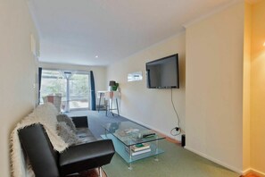 A modern living room with a glass coffee table, a black sofa, and a flat-screen TV mounted on the wall. - Peace and Love 2 BDR Townhouse West Melbourne (West Melbourne)