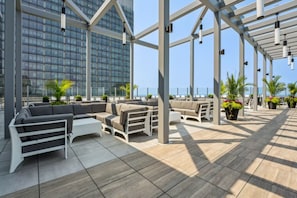 A rooftop terrace with outdoor seating, potted plants, and a view of a modern building. - Downtown Retreat - King Bed - Rooftop Pool + Hot Tub - Gym - Walkable (Cleveland)