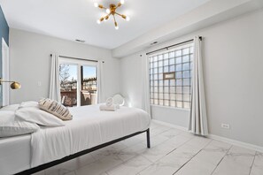 A bedroom with a bed, a window with curtains, a ceiling light fixture, and a view of the outside. - The Home Run: Modern 2BR Steps from Wrigley Field (Chicago)