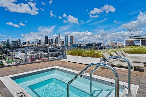 A rooftop pool with a city skyline view, lounge chairs, and a clear sky.