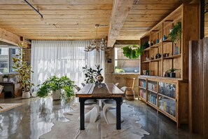 A wooden ceiling, a dining table with chairs, a bookshelf, and potted plants.