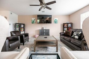 A living room with a ceiling fan, a flat-screen TV, leather sofas, a coffee table, and a cabinet with decorative items. - 4bd/2.5bth, 8 guests, Pet friendly (Dallas)