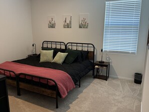 Een slaapkamer met een bed, nachtkastjes, een raam met zonwering en decoratieve wandkunst.