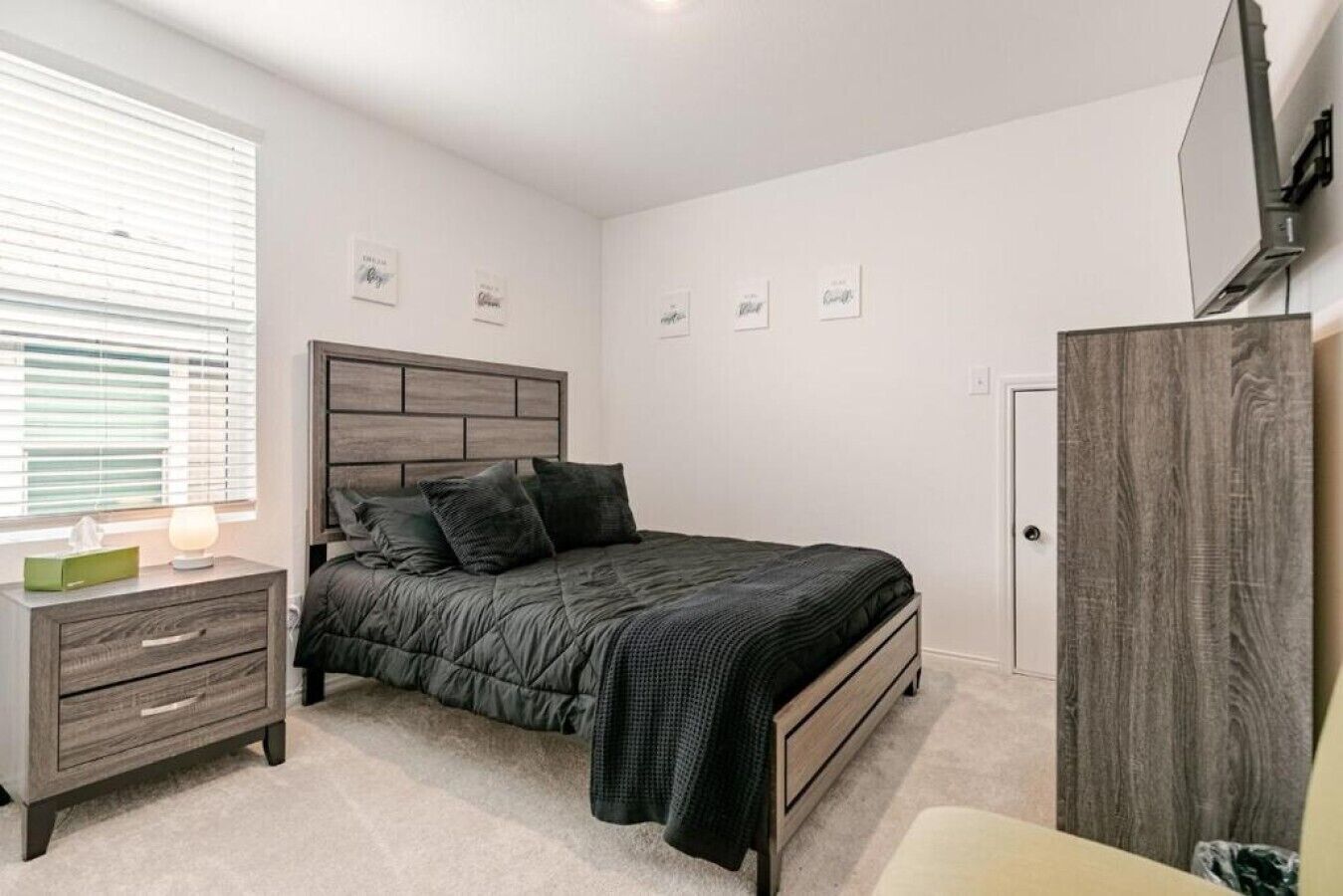 Un dormitorio con cama, mesita de noche, cómoda, televisor y puerta.