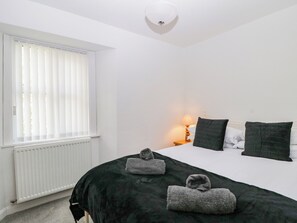 A bedroom with a bed, a nightstand, a lamp, and a window with blinds. - Fellfoot Cottage (Cockermouth)