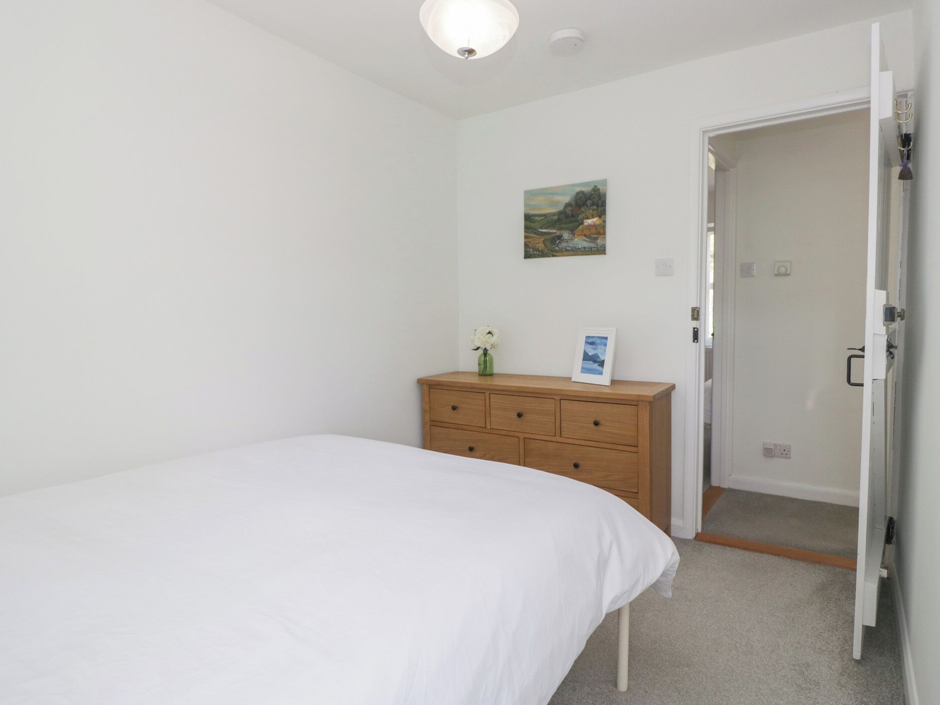 Un dormitorio con una cama individual, un aparador de madera, un cuadro en la pared y una puerta que da a otra habitación.