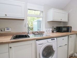 A compact kitchen with a washing machine, a microwave, and a sink. - Fellfoot Cottage (Cockermouth)