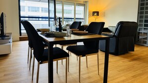 Un comedor moderno con una mesa de madera, sillas negras y vistas a un edificio a través de grandes ventanales.