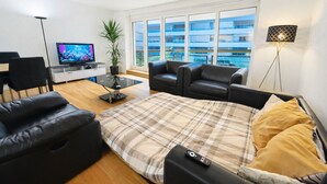 Una sala de estar moderna con sofá, mesa de centro, televisor y un ventanal con vistas a edificios.