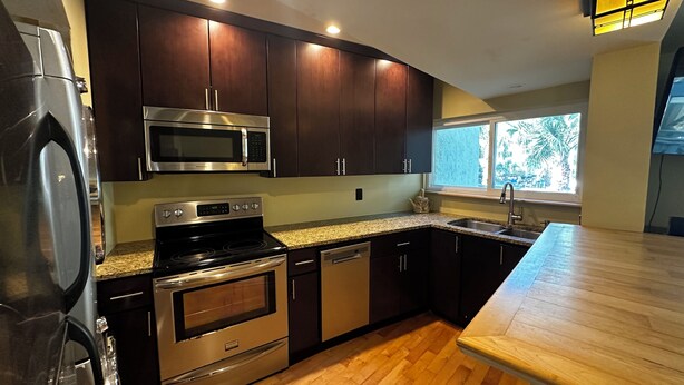 A modern kitchen with dark cabinets, stainless steel appliances, a granite countertop, and a window providing a view of greenery. - Beautiful 2-bedroom, 2 bathroom villa in South Forest Beach. Hilton Head Island (Hilton Head Island)