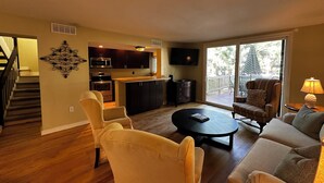 A living room with a sofa, armchairs, a coffee table, a kitchen with dark cabinets, a TV, and a sliding glass door leading to an outdoor area. - Beautiful 2-bedroom, 2 bathroom villa in South Forest Beach. Hilton Head Island (Hilton Head Island)