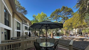 A wooden deck with a table and chairs, a striped umbrella, and a pool in the background. - Beautiful 2-bedroom, 2 bathroom villa in South Forest Beach. Hilton Head Island (Hilton Head Island)