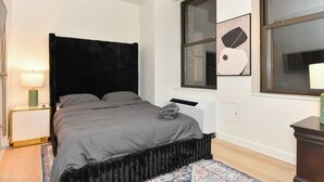 A bedroom with a bed, a nightstand, a radiator, a window, and a wall-mounted artwork. - Sleek 2BR Oasis in NYC Financial District (New York)