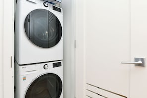 Une machine à laver et un sèche-linge superposés dans une buanderie aux murs blancs.