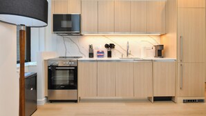 A modern kitchen with wooden cabinets, a built-in oven, a microwave, and a sink. - Sleek 2BR Oasis in NYC Financial District (New York)