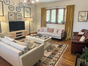 A living room with a sofa, armchair, TV, and decorative wall art. - The Lady Rothschild Stables (Peterborough)