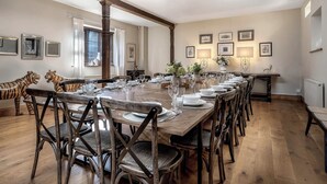 Uma sala de jantar com uma longa mesa de madeira posta para refeição, cercada por cadeiras de madeira com assentos trançados.