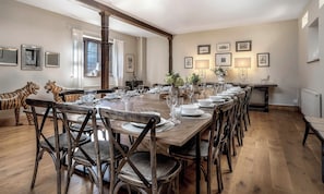 A dining room with a long wooden table set for a meal, surrounded by wooden chairs with woven seats. - The Lady Rothschild Stables (Peterborough)